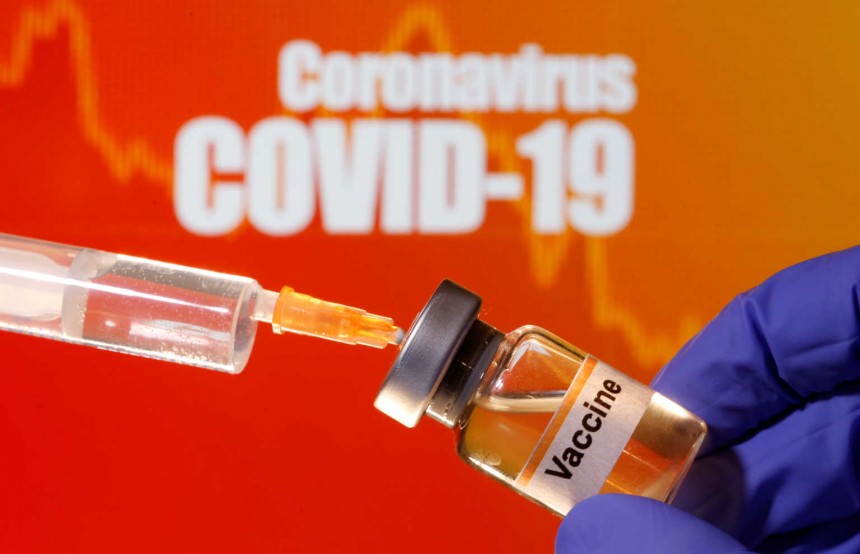 A small bottle labeled with a "Vaccine" sticker is held near a medical syringe in front of displayed "Coronavirus COVID-19" words in this illustration taken April 10, 2020. REUTERS/Dado Ruvic/Illustration